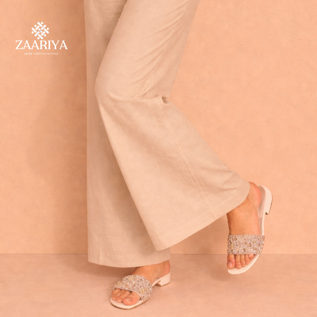 Woman wearing beige pants and embellished sandals on a peach background with Zaariya branding.