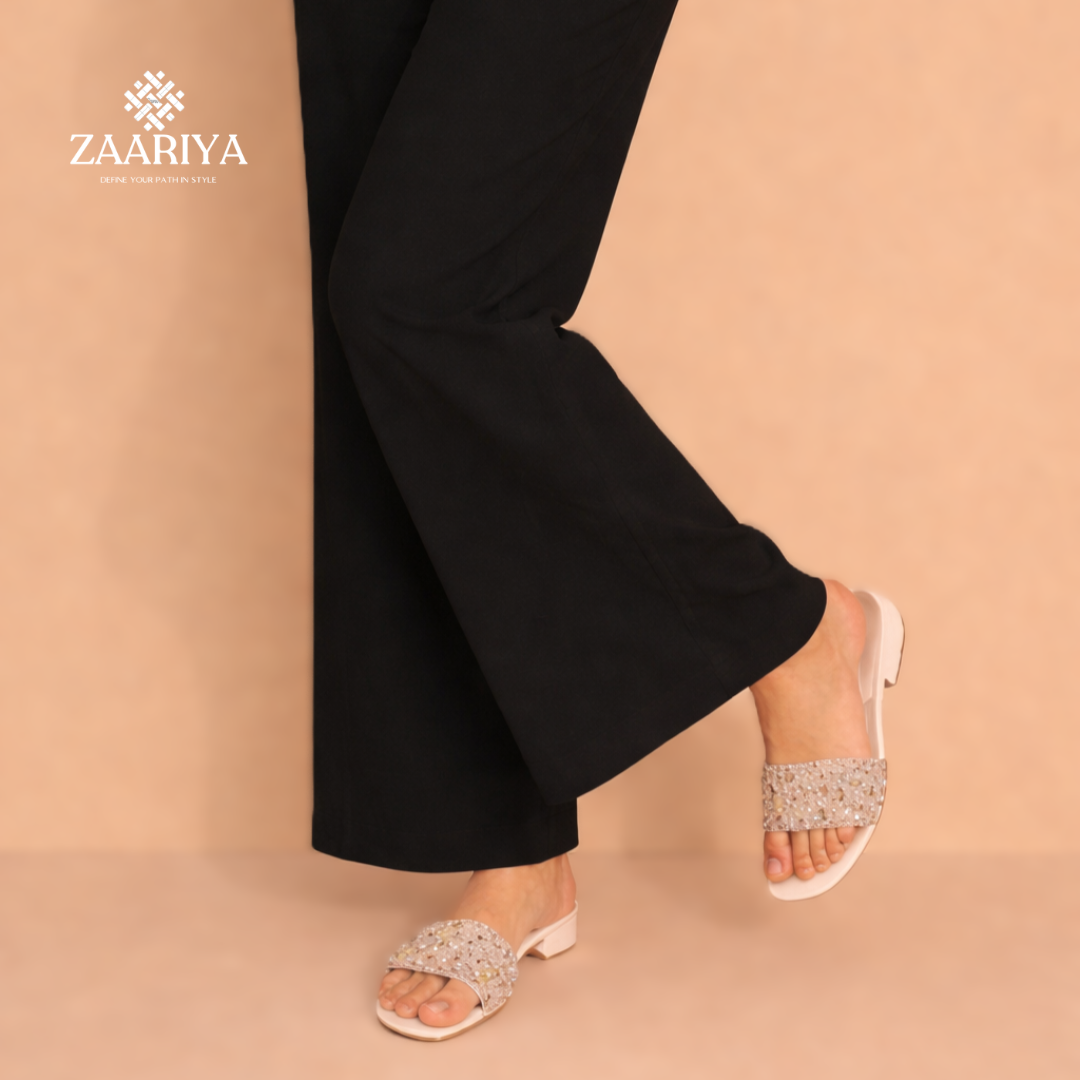 Person wearing black pants and sparkling sandals on a beige background with Zaariya logo.